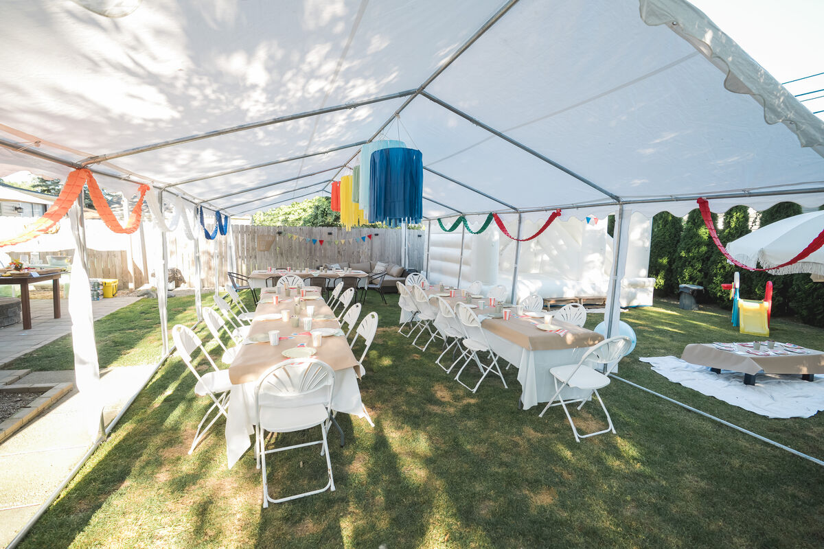 Decorated tent with tables, streamers, and bounce house at backyard party